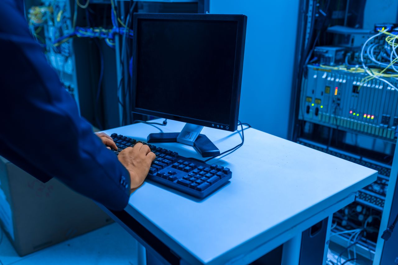 about-us An IT professional operates a computer in a server room, managing network systems and connected devices.